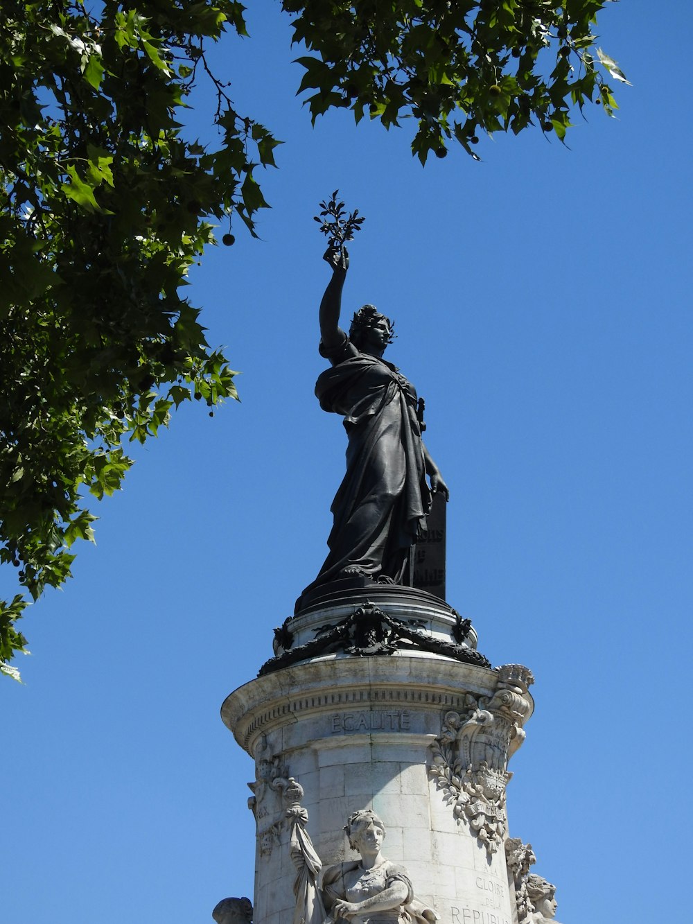 statue of man holding book under blue sky during daytime