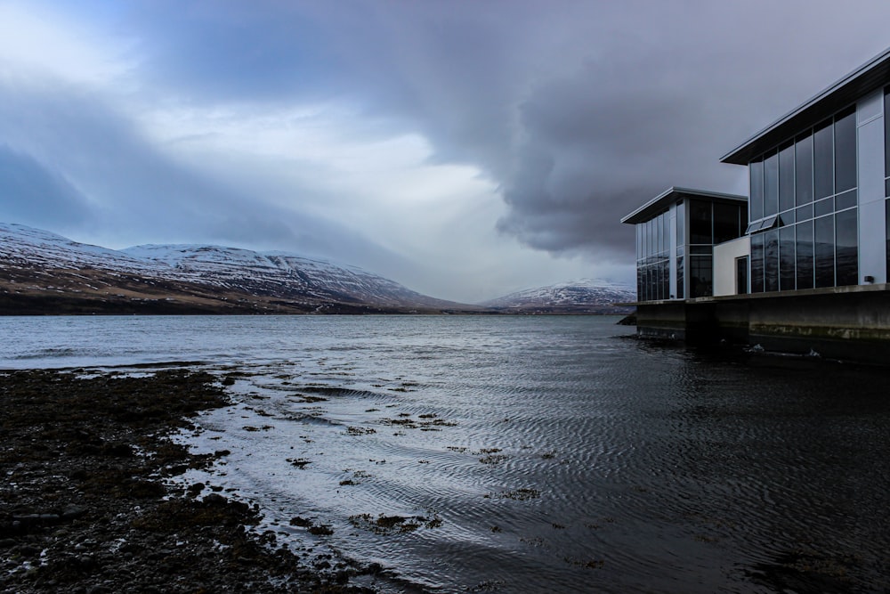 white wooden house on lake near mountains under white clouds and blue sky during daytime