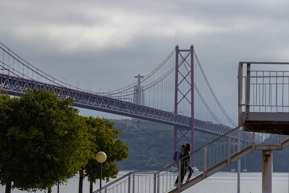 man in black jacket and black pants standing on bridge during daytime