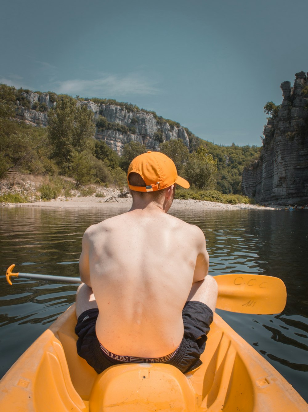 Homem de topless vestindo shorts laranja e preto andando de caiaque laranja no lago durante o dia