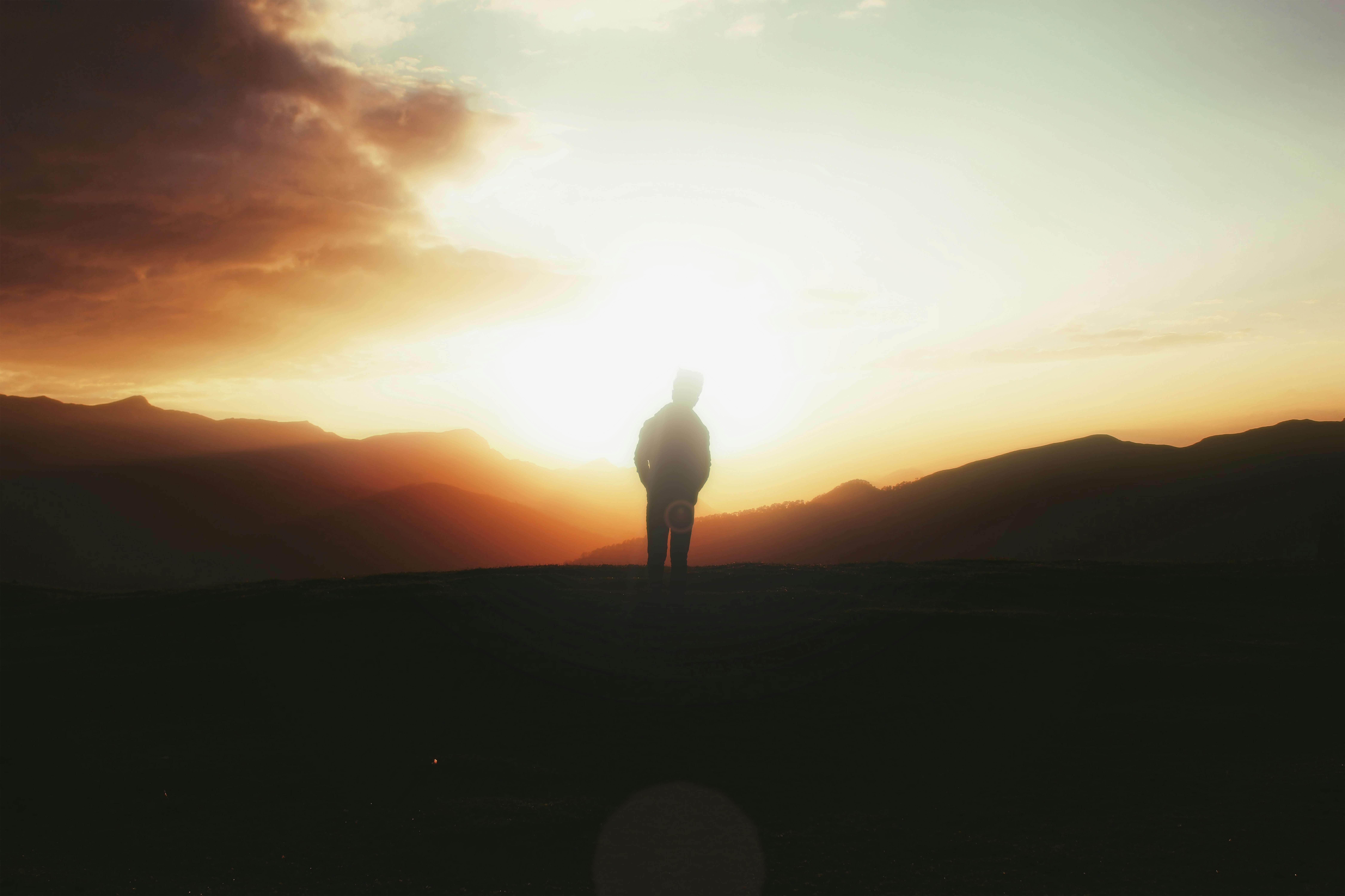 Mountaineer silhouetted against vast alpine panorama at sunset