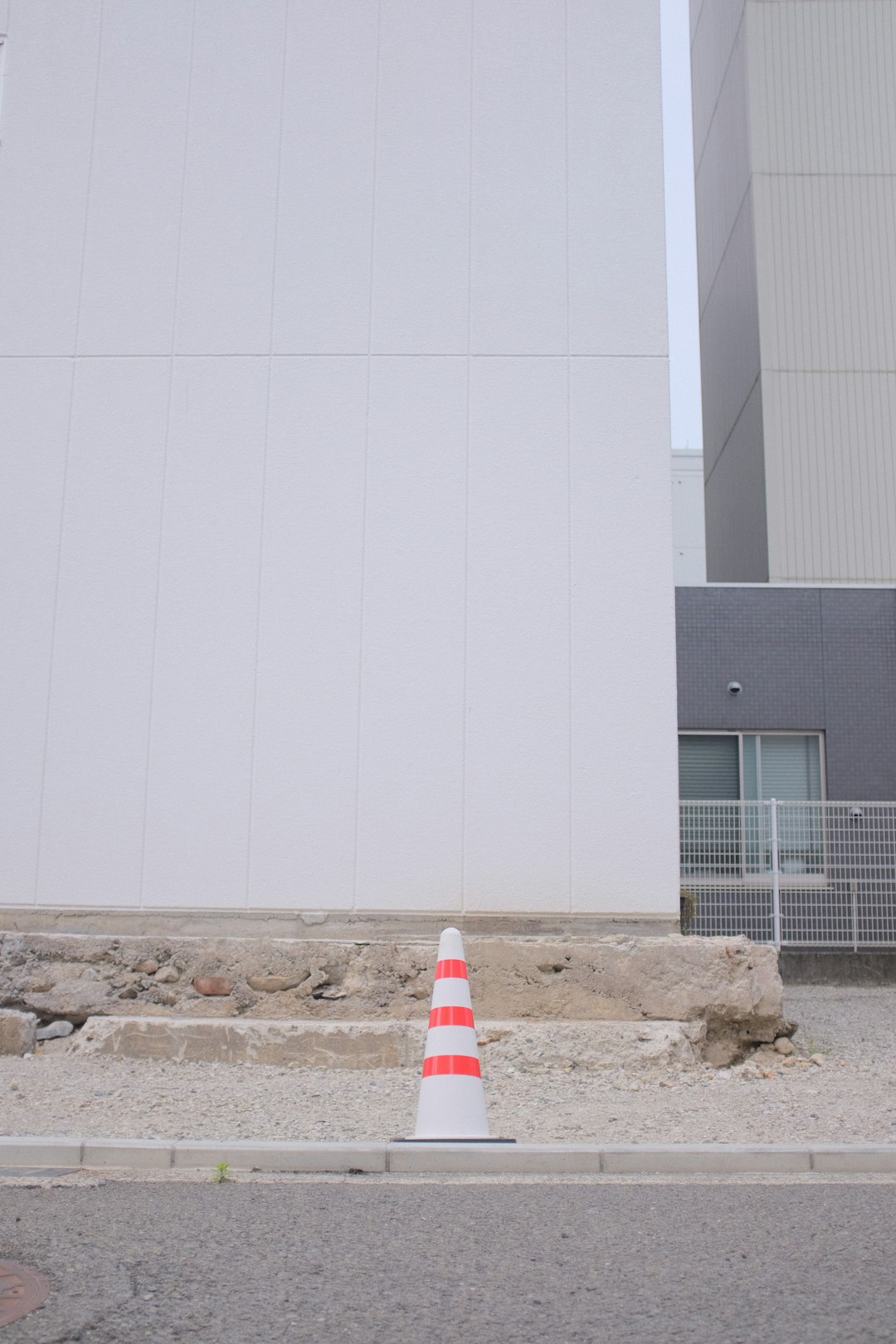 white and red striped traffic cone on brown sand near white building during daytime