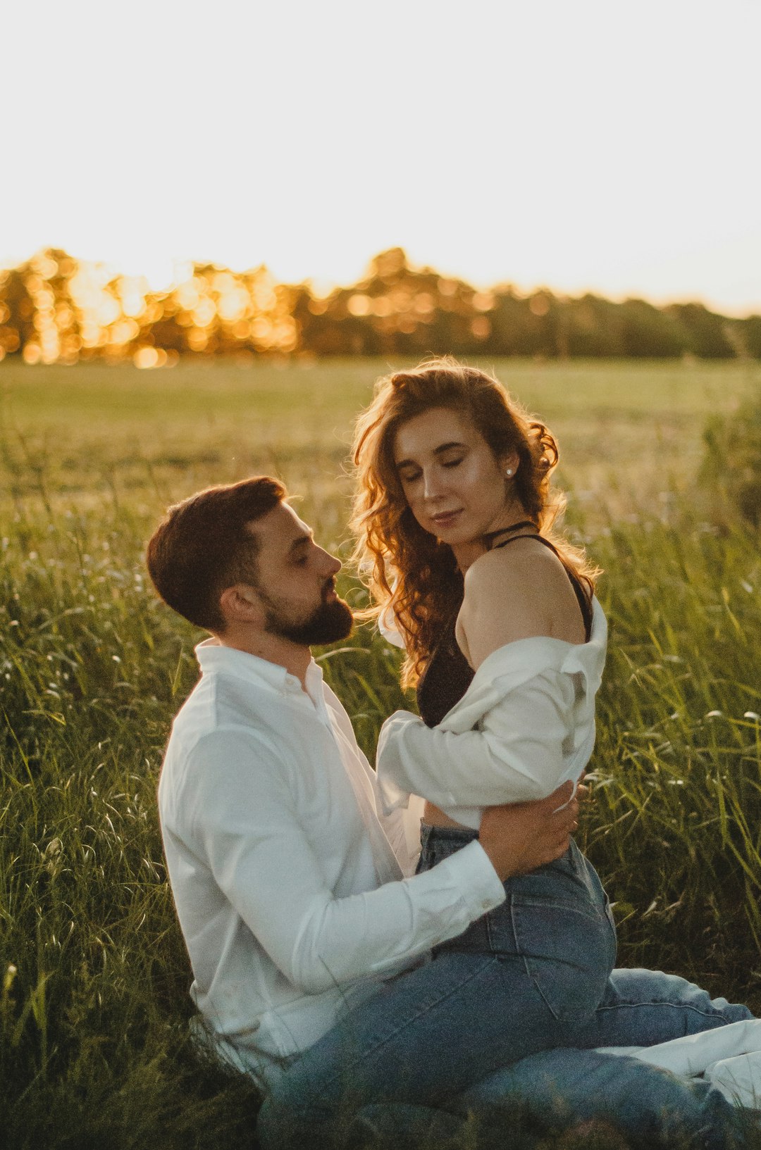 man in white dress shirt kissing woman in blue denim jeans on green grass field during