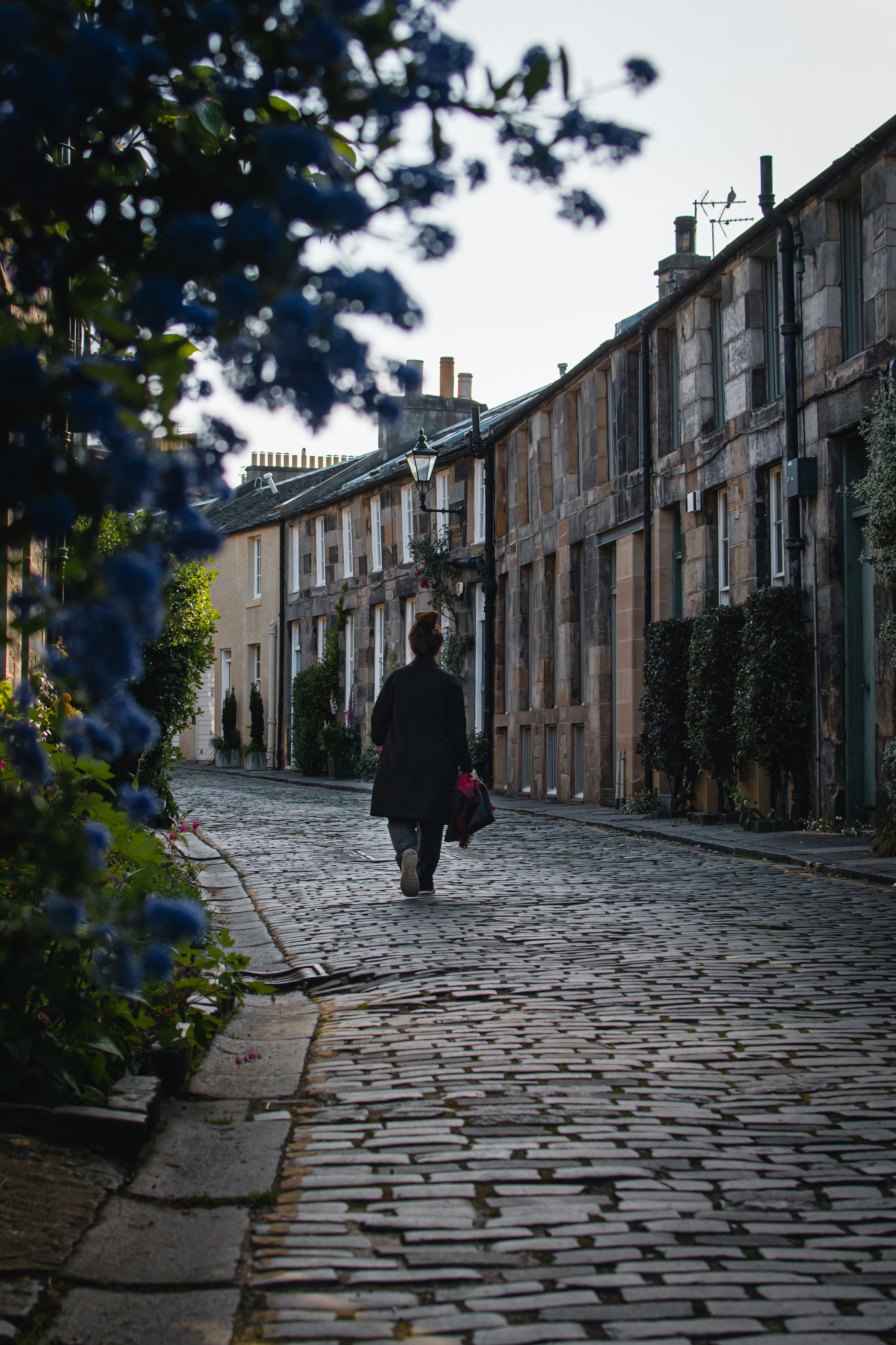 personne en manteau noir marchant sur le trottoir pendant la journée