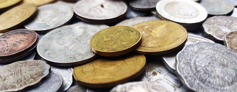 A close-up of vintage coins and old banknotes spread on a wooden table, symbolizing the history of money.