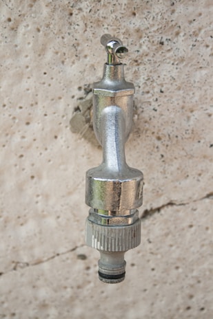 A metallic outdoor faucet attached to a textured stone wall, with a shiny chrome finish reflecting light.