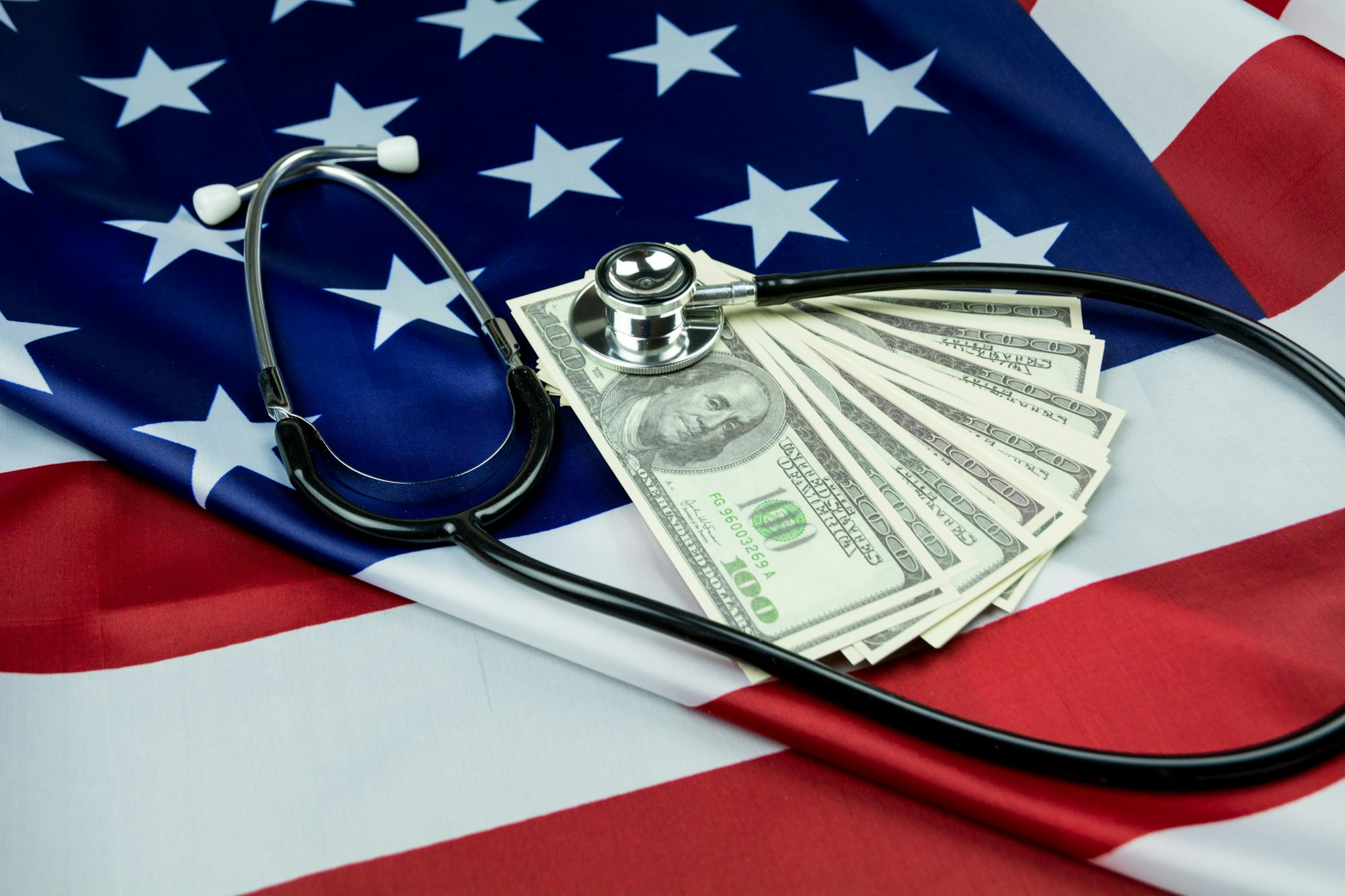 Close-up Of Stethoscope On Us Currency And American Flag