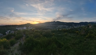 A scenic view of the village landscape with hills in the background at sunset.