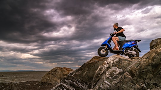 man in red shirt and blue denim jeans sitting on black and white motorcycle on gray in Rimouski Canada