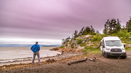 man in blue jacket and white pants standing on seashore during daytime in Kamouraska Canada