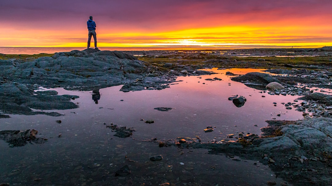 man in black shirt standing on rocky shore during sunset