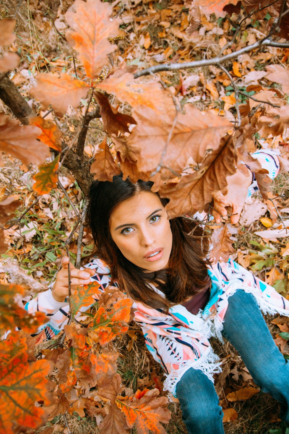 woman in white and blue floral long sleeve shirt lying on brown leaves