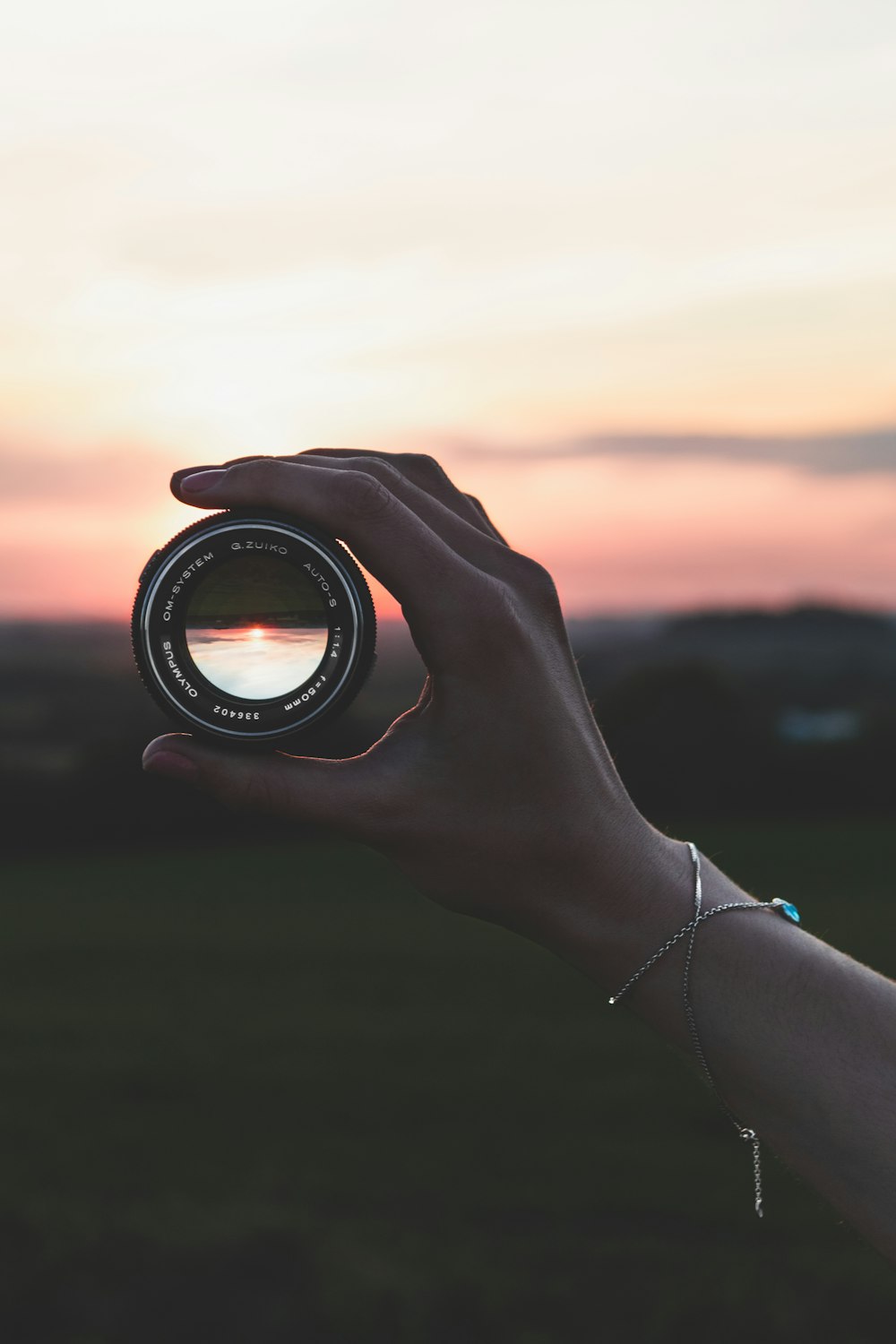 Persona che tiene l'obiettivo rotondo nero della macchina fotografica durante il tramonto