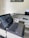 A modern laptop is open on a desk, displaying a web page. The setup includes a printer to the right, other office supplies, and a piece of colorful art on the wall. The desk and walls have a clean and organized appearance.
