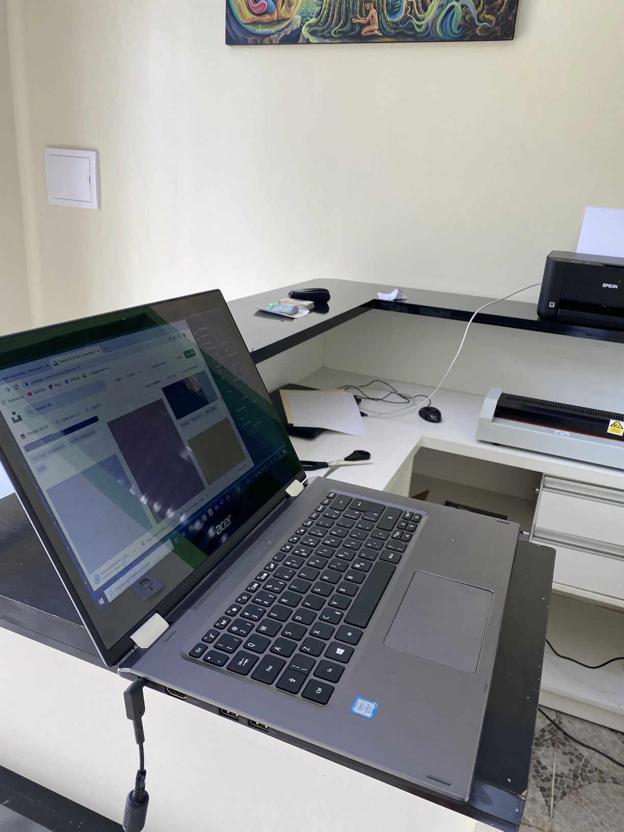 A friendly technician setting up a printer driver on a laptop with gaming gear and design sketches in the background.