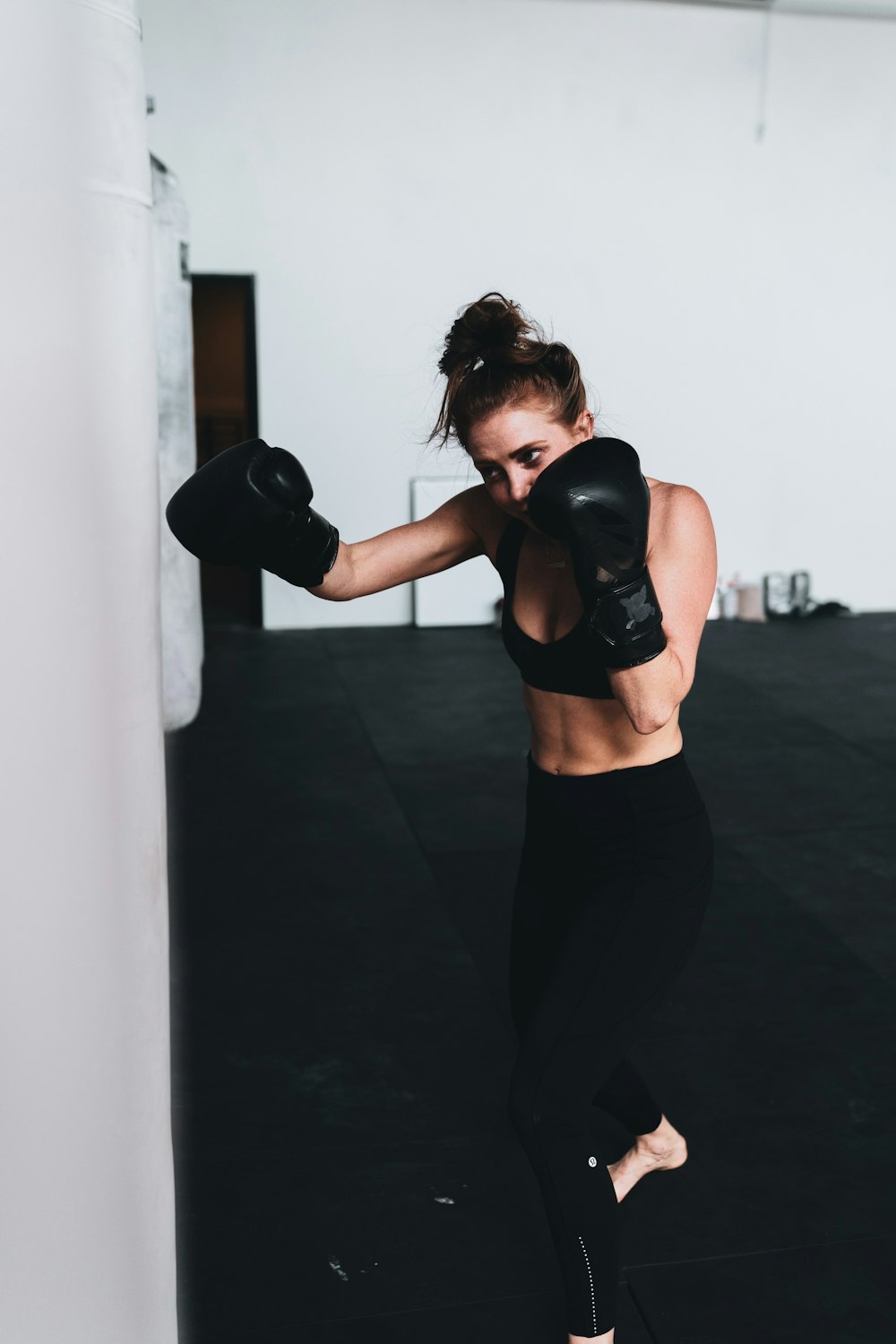 mulher no sutiã esportivo preto e leggings pretas usando luvas pretas de boxe