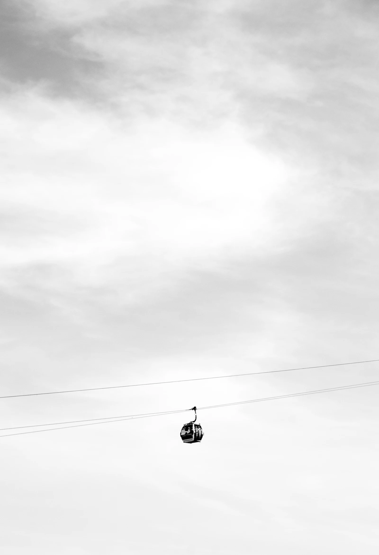 Photograph of A single London Cable Car cabin suspended against a broad, pale clouded sky.