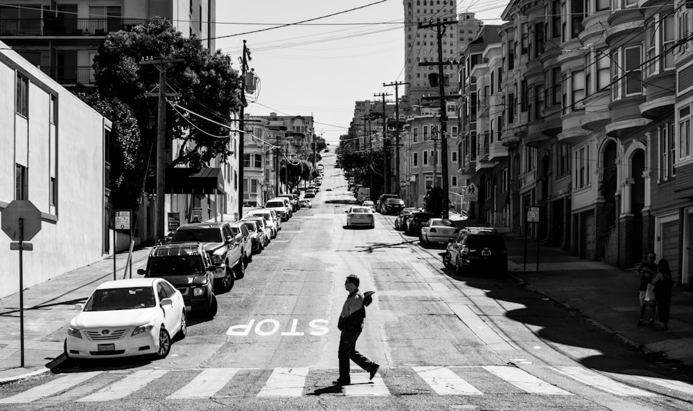 grayscale photo of man walking on pedestrian lane