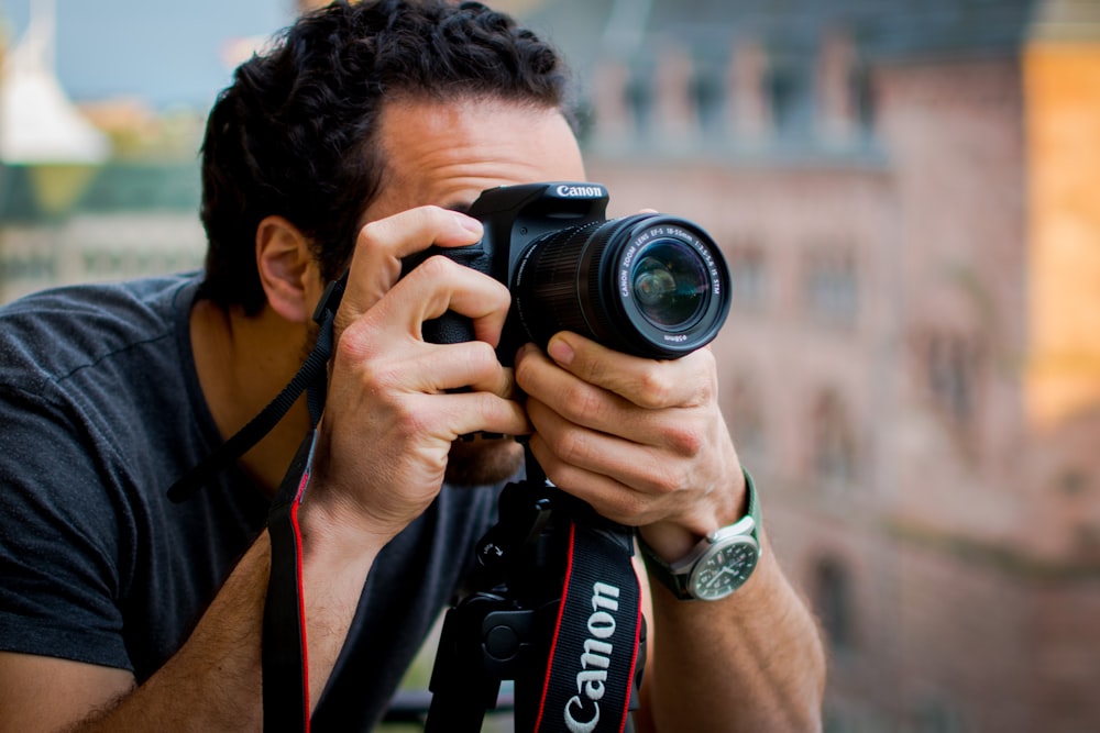 man in red shirt holding black nikon dslr camera