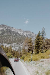 A scenic view of a taxi winding along a mountain road with pine trees and distant peaks in the background.