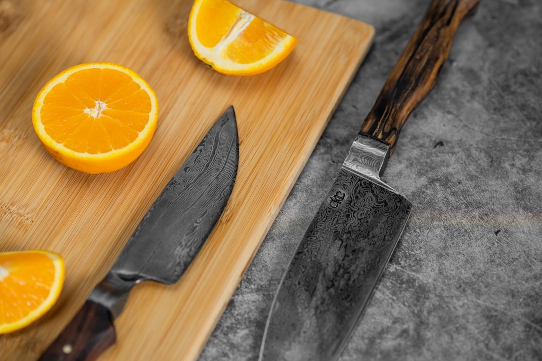 sliced orange fruit beside silver bread knife on brown wooden chopping board