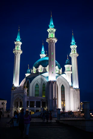 The majestic Sultan Qaboos Grand Mosque illuminated against a twilight sky, showcasing intricate Islamic architecture.