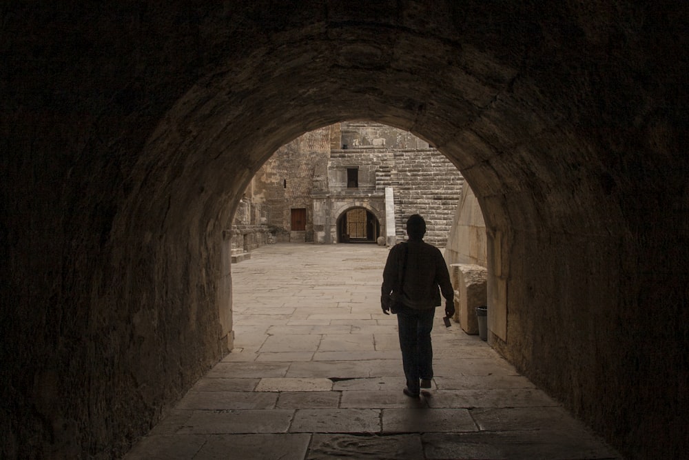 man in black jacket standing on brown brick hallway