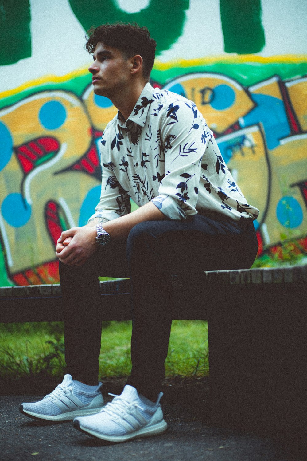 man in white and black floral button up shirt sitting on black wooden bench