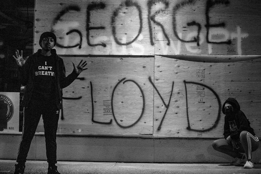 man in black hoodie standing beside wall with graffiti