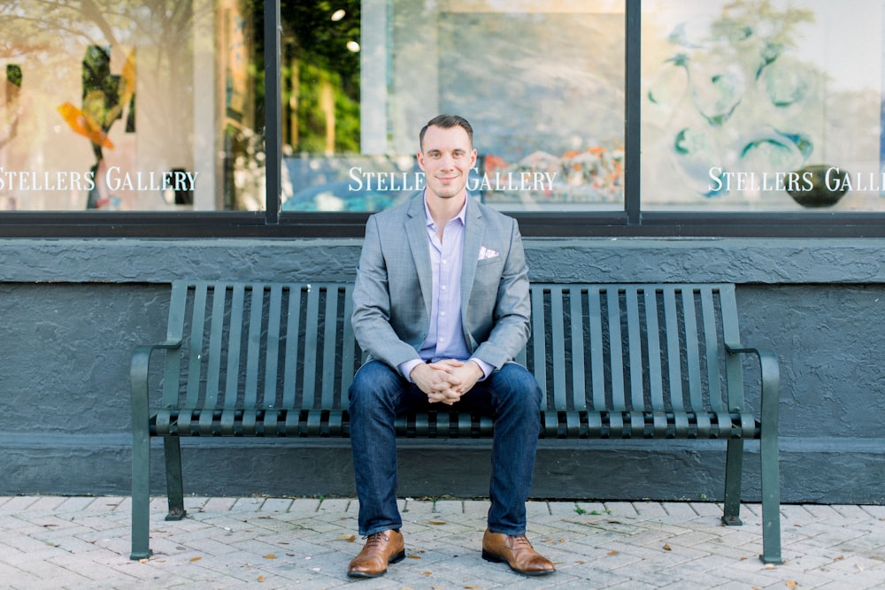 man in gray suit jacket sitting on black bench