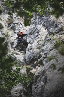A climber carefully ascending a steep rock face with a safety rope.