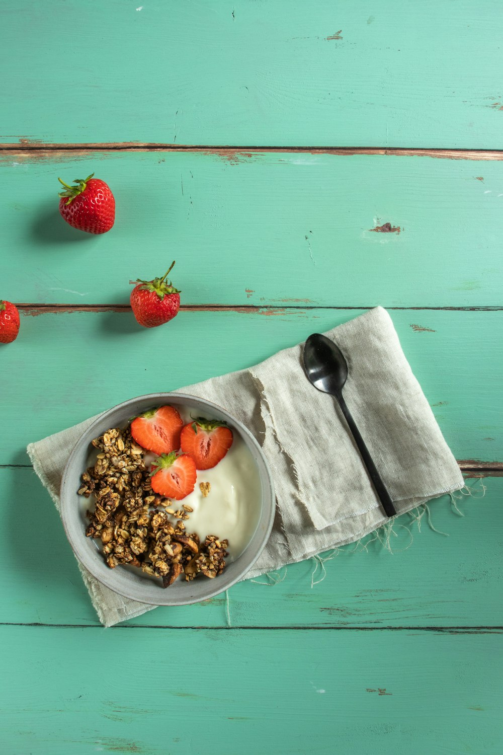 strawberries and blueberries in white ceramic bowl beside stainless steel spoon