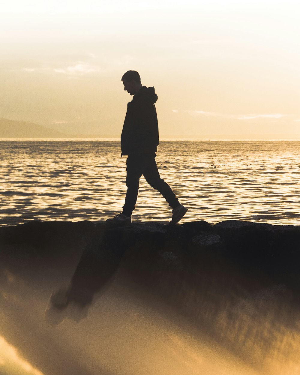 silhueta do homem de pé na rocha perto do mar durante o pôr do sol
