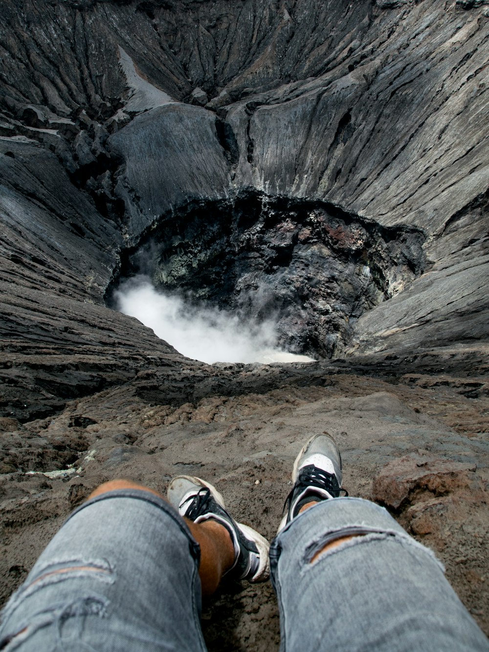 person in blue denim jeans and brown hiking shoes sitting on rock formation during daytime