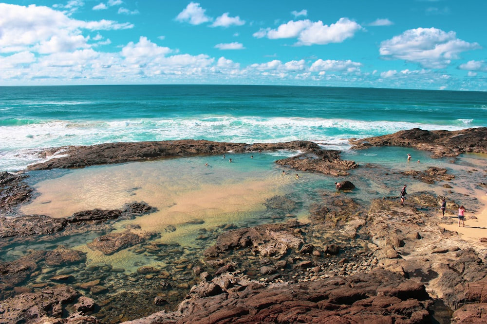 brown and black rock formation on sea under blue and white cloudy sky during daytime