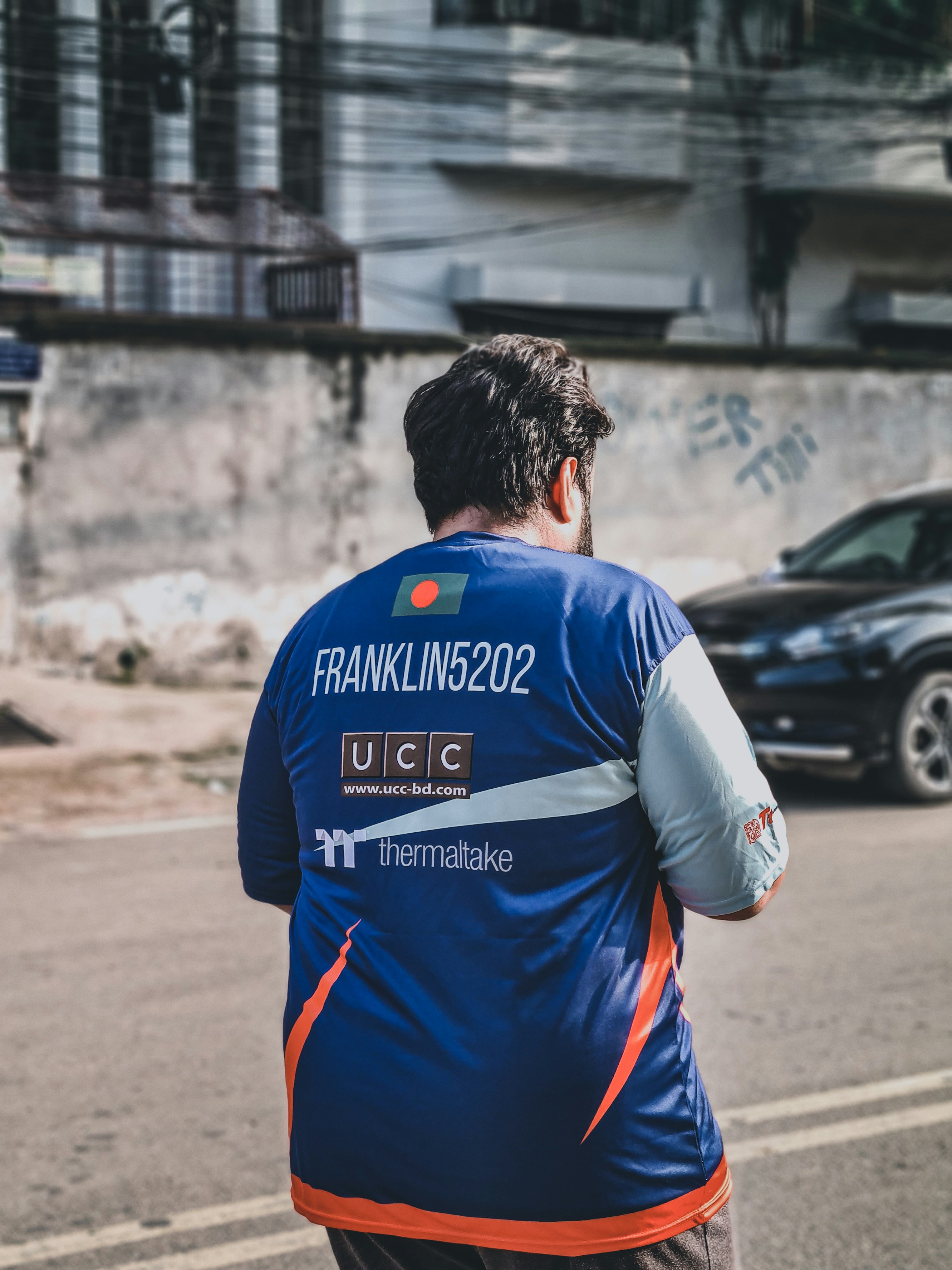 man in blue and white adidas soccer jersey standing on road during daytime