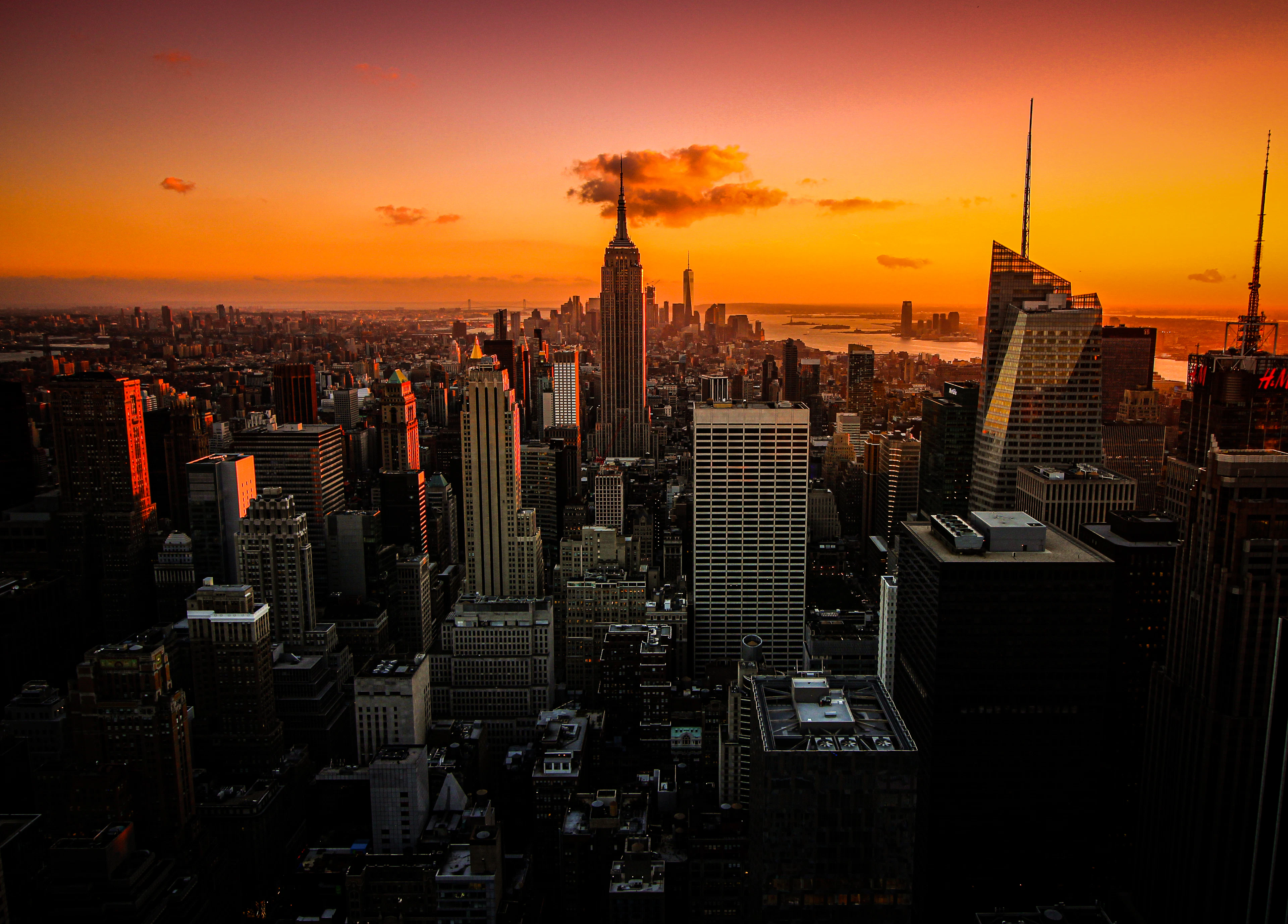 Manhattan at sunset from above, the Empire State Building standing out of the grid against an orange sky