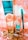 A collection of beauty products and accessories arranged on a decorative surface. The items include a tall metallic gold and turquoise bottle, a smaller matching bottle labeled as nail lacquer, a turquoise eyeliner pencil, and a set of large, circular, golden earrings. The background has an ornate, floral pattern in shades of peach and white.