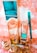 A collection of beauty products and accessories arranged on a decorative surface. The items include a tall metallic gold and turquoise bottle, a smaller matching bottle labeled as nail lacquer, a turquoise eyeliner pencil, and a set of large, circular, golden earrings. The background has an ornate, floral pattern in shades of peach and white.