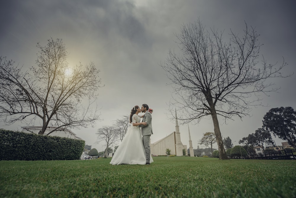 a bride and groom standing in the grass in front of a church
