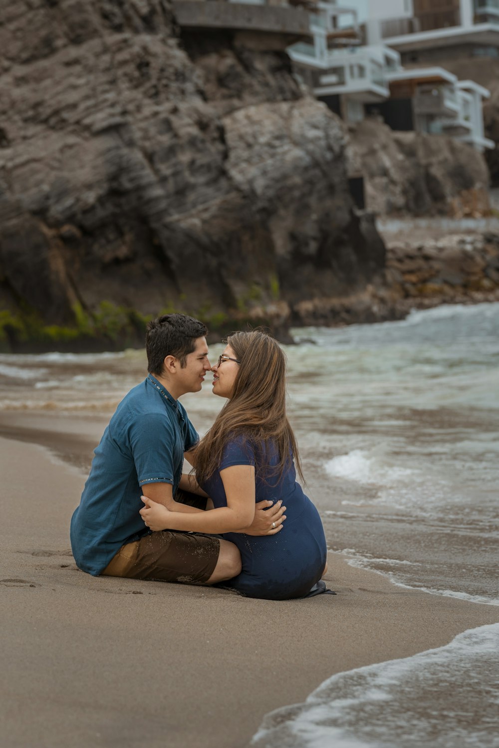 a man and woman sitting on the beach kissing