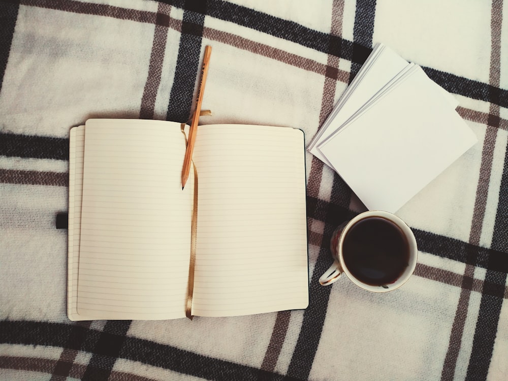 white book beside white ceramic mug on white and black plaid textile