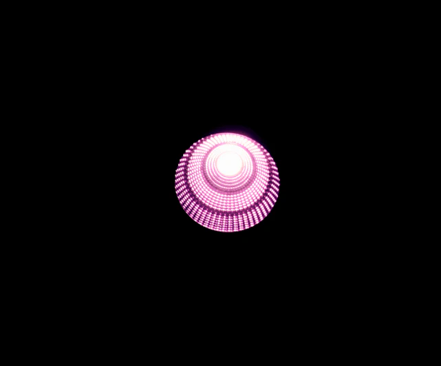 A large rotating cassette emoji glowing with neon pink light against a cosmic black background.