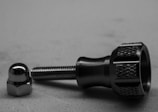 A metal component with a threaded bolt and a knurled grip lies next to a shiny, reflective cap or nut on a flat surface.