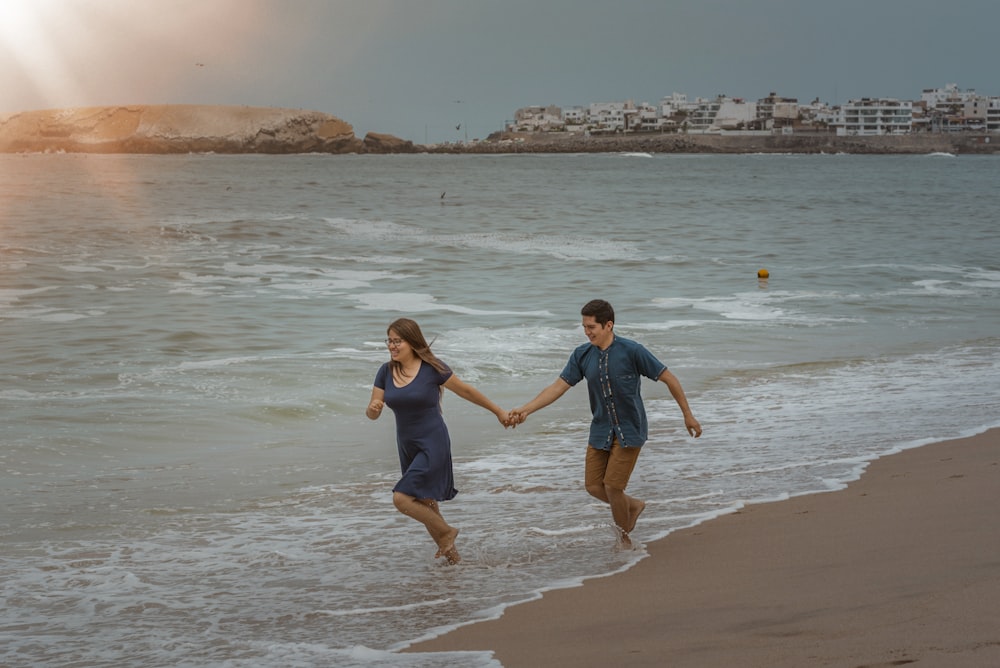 a man and a woman holding hands walking along the beach