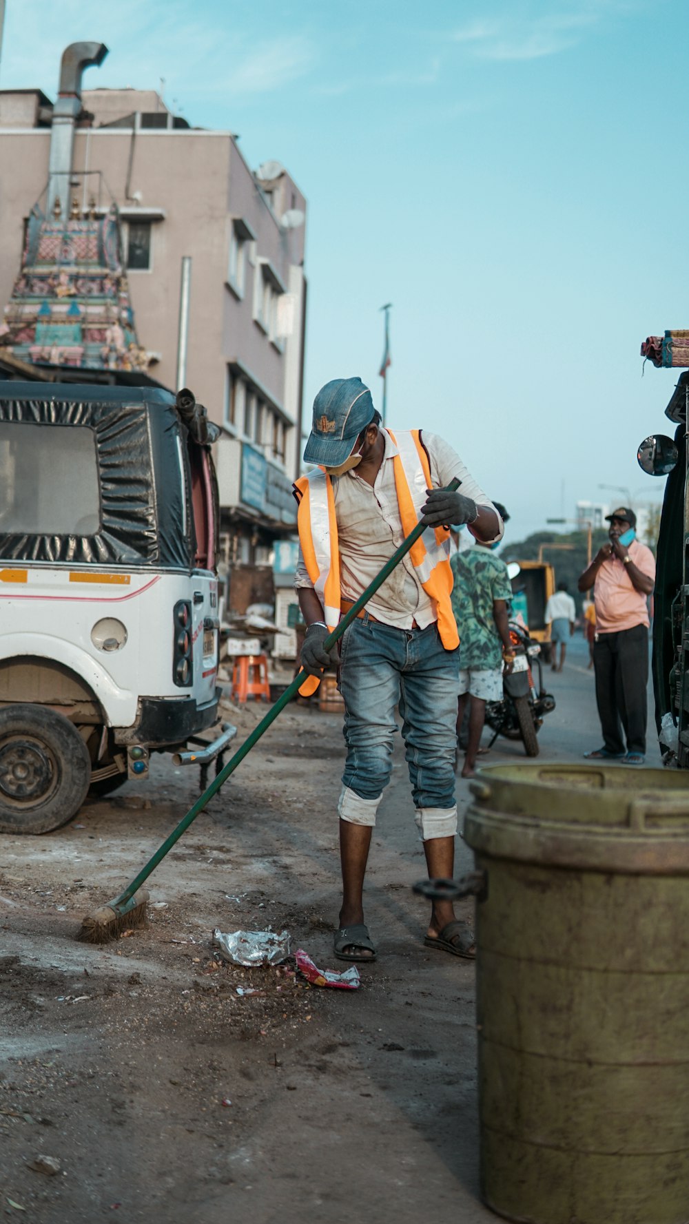 man in orange vest and blue denim jeans standing on white truck during daytime