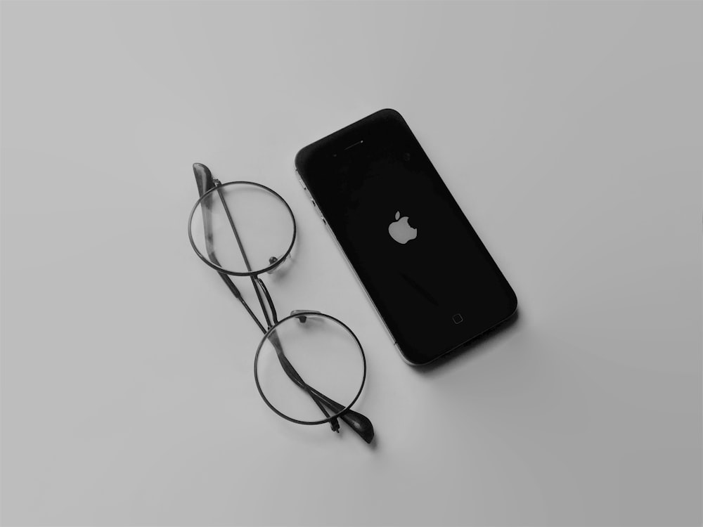 black iphone 4 beside black framed eyeglasses
