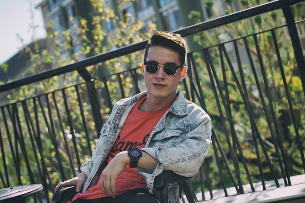 man in blue denim jacket sitting on black metal bench during daytime