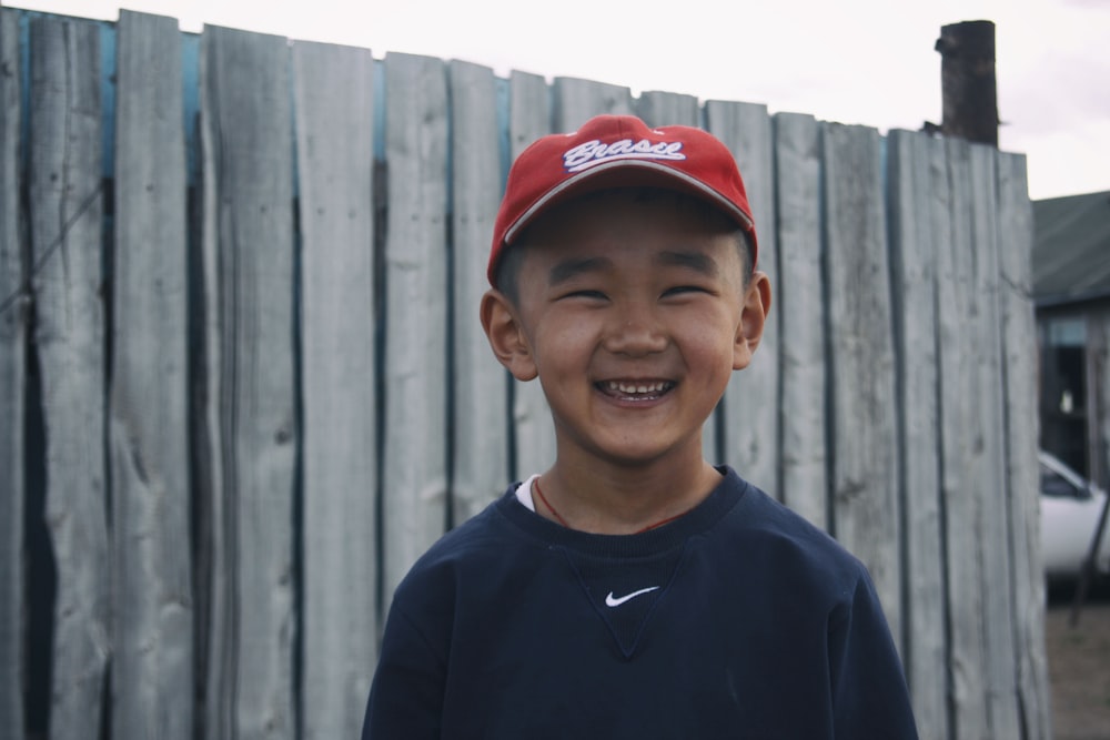 boy in blue crew neck shirt and red cap smiling