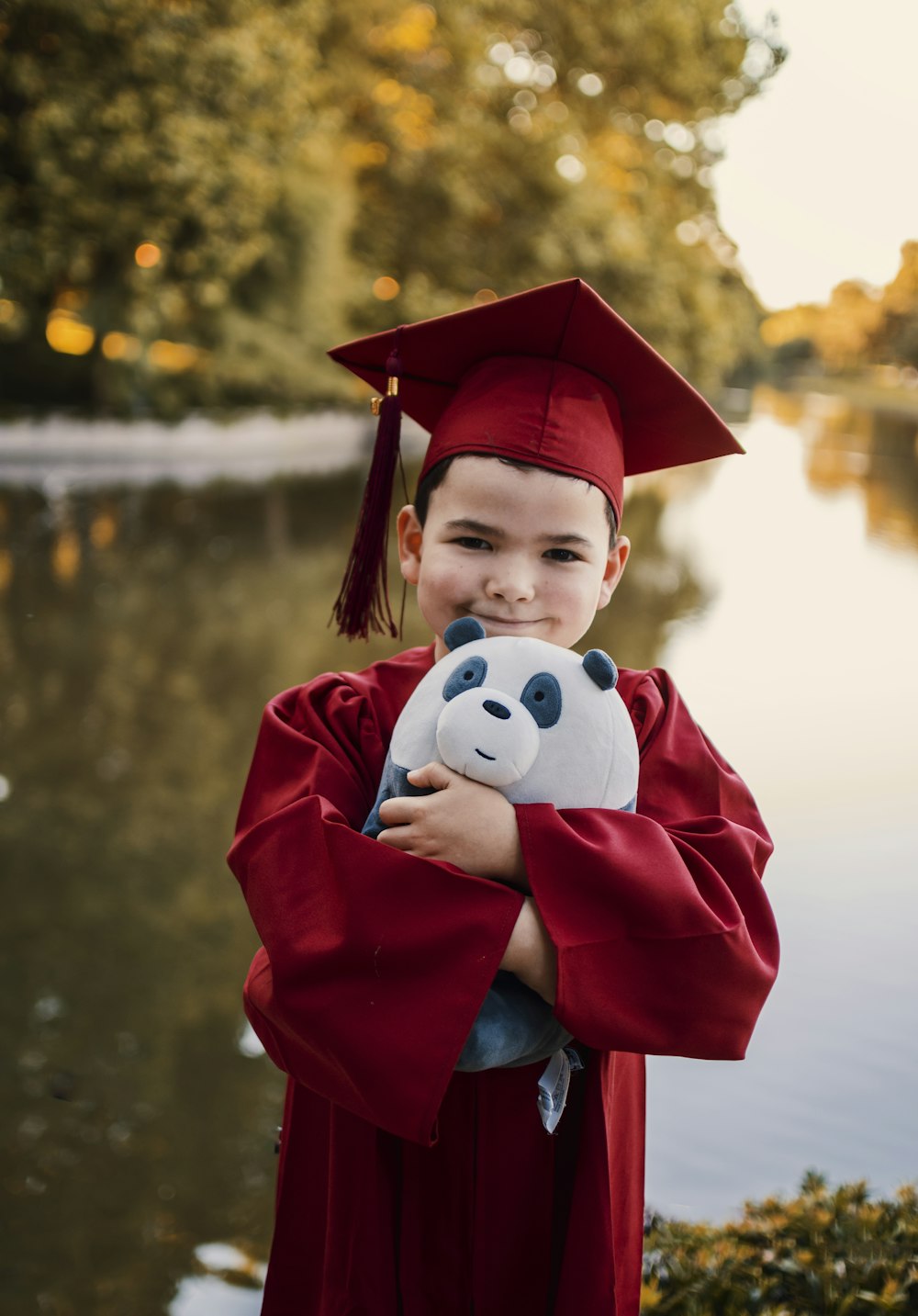 boy in red academic dress with white and black panda plush toy